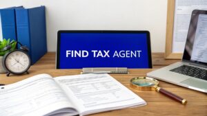 Find tax agent message on computer screen with paperwork, clock, and laptop on a wooden desk.